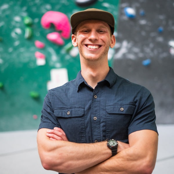 Gabe Linderman standing with arms crossed in from of indoor climbing wall.